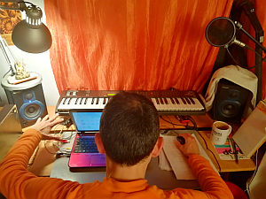 Photo of Dusum Sangtong at his home studio, going to compose new music playing a keyboard while having a cup of tea
